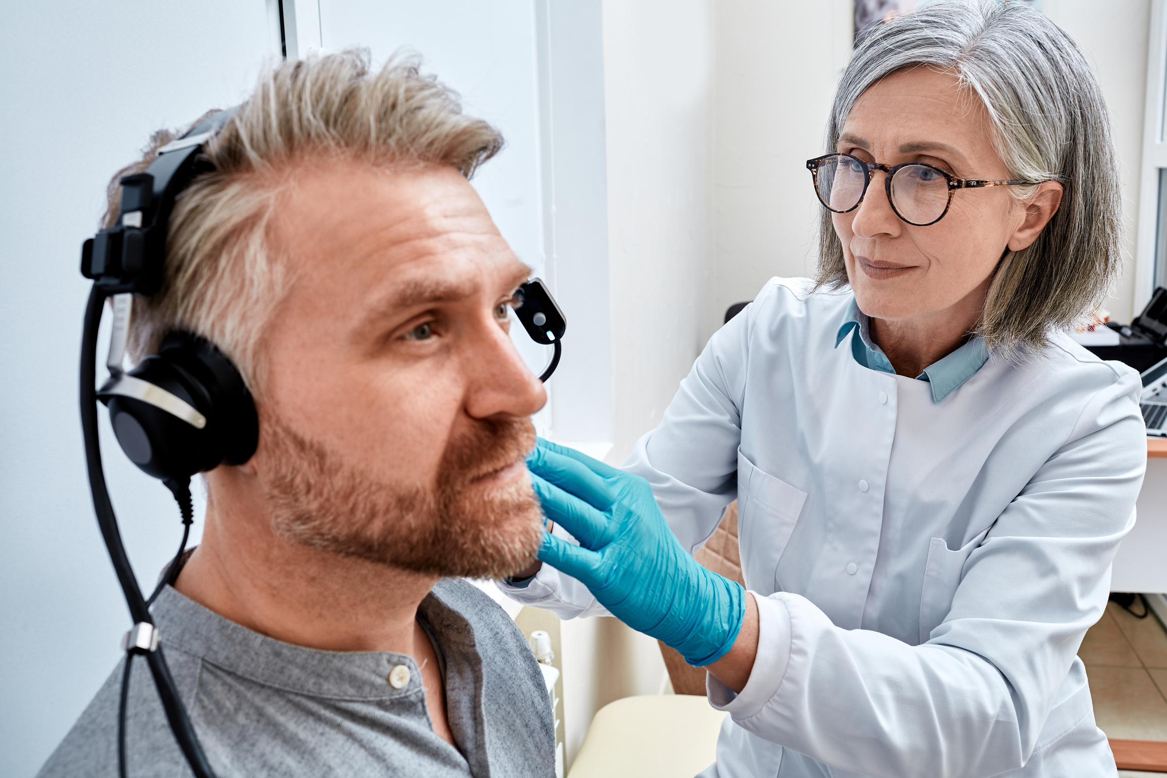 Mature man receives tympanometry with audiologist using tympanometer at audiology clinic. Hearing check-up, impedance audiometry